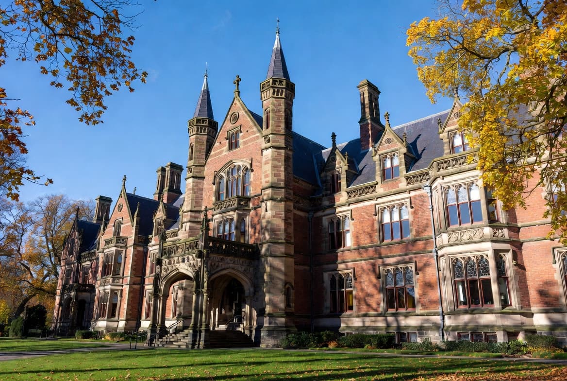 Historic red-brick university building framed by autumn trees